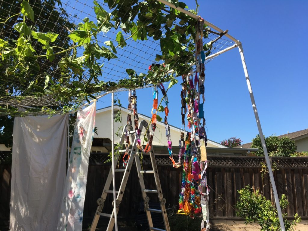 A sukkah made of PVC pipe, decorated with vines, sheets, and paper chains